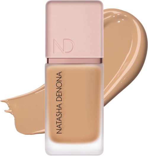 Eine Foundation-Flasche mit einem beige Creme-Strich im Hintergrund, beschriftet Natasha Denona, mit pinker Kappe.