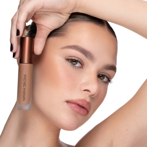 Eine Frau mit klarer Haut hält eine beige Lippenstift near ihrem Gesicht.