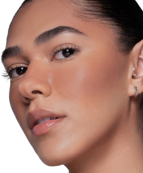 Nahaufnahme einer Frau mit glatter Haut, dunklem Haar und natürlichem Make-up. Sie trägt Ohrringe und leicht geöffnete Lippen.