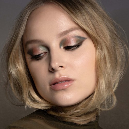 Eine Frau mit kurzen blonden Haaren und eleganter Augen-Make-up schaut nach unten vor neutralem Hintergrund.