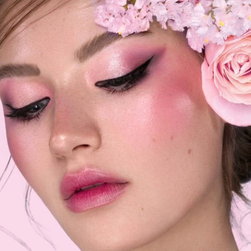 Eine Frau mit rosa Make-up, schwarzem Eyeliner und Blumenkrone aus rosa und weißen Blumen.
