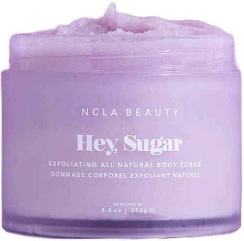 En lila burk med NCLA Beauty-kroppsskrubb som heter Hey, Sugar, med skrubb ovanpå.