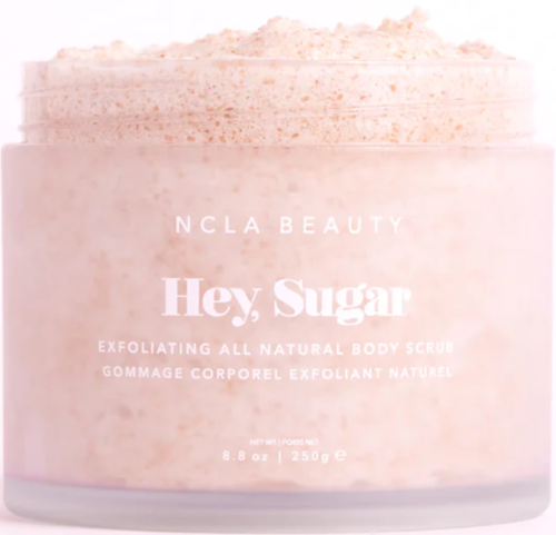 Ein rosa Behälter mit einem Körperpeeling namens 'Hey, Sugar' von NCLA Beauty, mit Beschreibung der exfolierenden Natur.