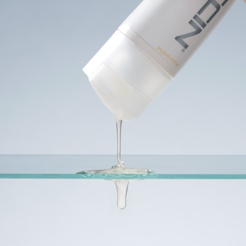 Een witte fles giet een heldere vloeistof op een glazen oppervlak.