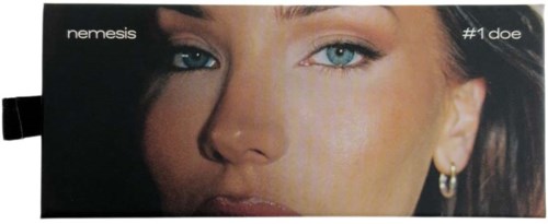 A close-up of a woman's face with blue eyes and earrings, with black and white background. Includes text 'nemesis' and '#1 doe'.