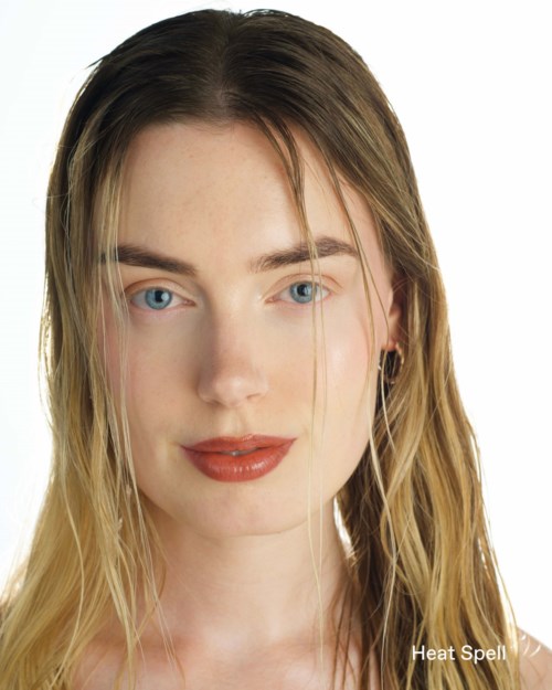 A young woman with blond hair, blue eyes, and red lipstick, smiling softly with a neutral background.