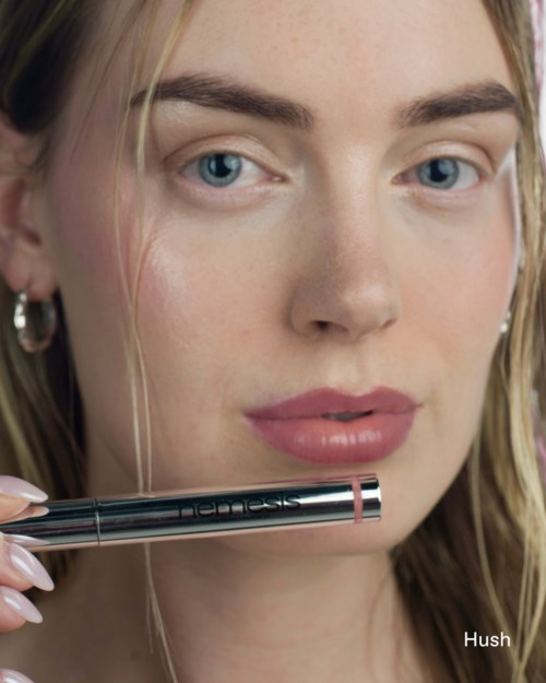 A woman with blue eyes and blonde hair holding a sleek pen near her face.