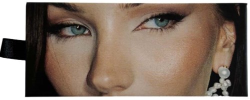 Close-up of a woman's face with striking eyes, makeup, and pearl earrings in a rectangular frame.