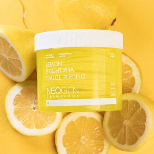 Een gele potje van Neogen Lemon Bright PHA Gauze Peeling omringd door citroenpartjes. Heldere en frisse sfeer.