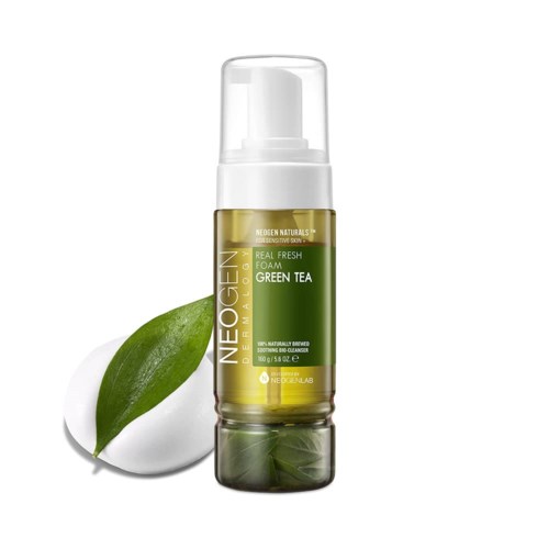 Huidverzorgingsproduct in doorzichtige fles met pomp, gemarkeerd 'Green Tea,' naast groene thee blad en een flinke dot schuim.