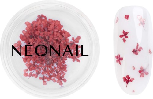 Pink flower-shaped nail decorations next to a nail with pink flowers on a white background.
