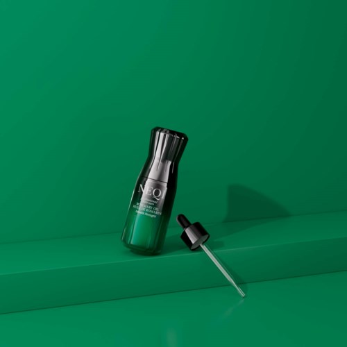 Een huidverzorgingsproductfles met pipet, op een groene achtergrond en oppervlakte.