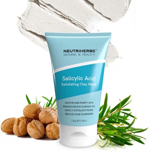 Eine blaue Tube mit Neutriherbs Salicylsäure Peeling Clay Maske neben Nüssen und grünen Pflanzen.