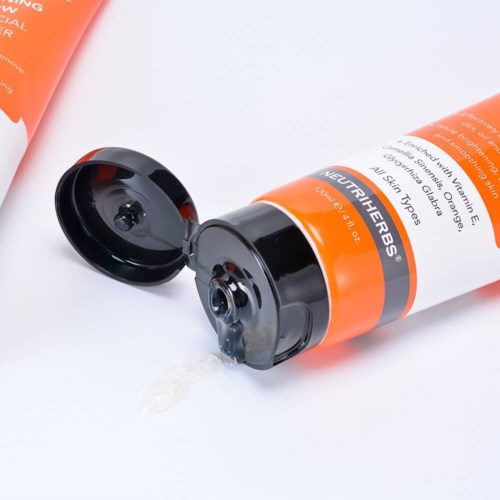 Ein Tube mit orange und schwarzem Etikett, offener Deckel und Flüssigkeit läuft aus.