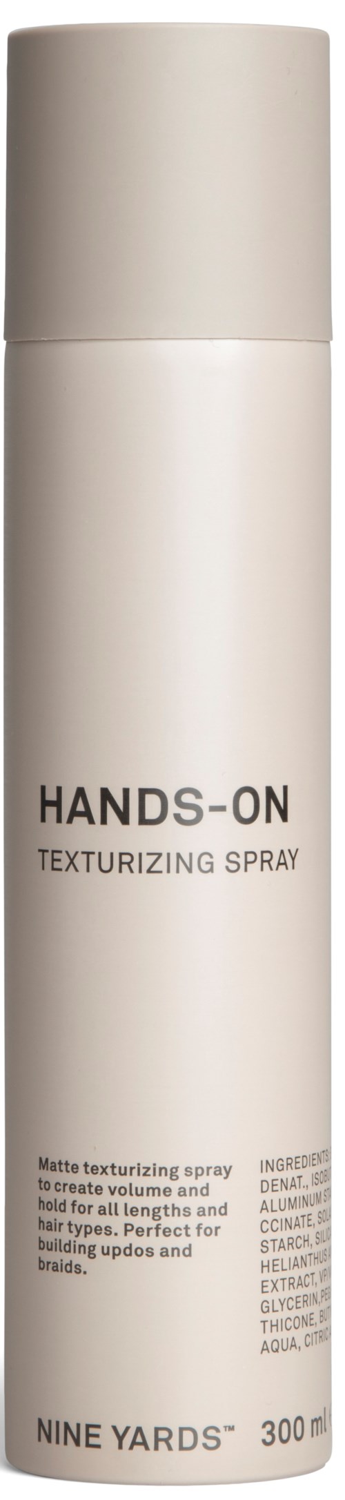 Biała cylindryczna butelka z sprayem z napisem "HANDS-ON TEXTURIZING SPRAY" i małym tekstem opisującym jego użycie.