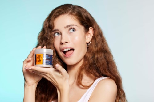 Een vrouw met lang, krullend rood haar houdt een pot vast, kijkt omhoog en glimlacht nadenkend.