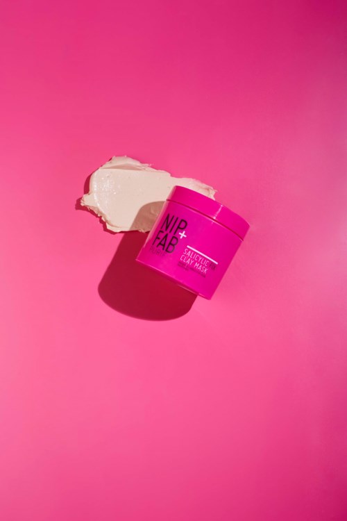 Een roze container met huidverzorgingsroom met wat room erop gestrooid op een roze achtergrond.
