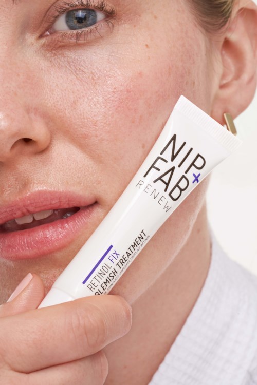 Close-up van een vrouw die een huidverzorgingsproduct dicht bij haar gezicht vasthoudt, zichtbaar deel van haar oog en lippen. Het product is gelabeld 'NIP+FAB'.