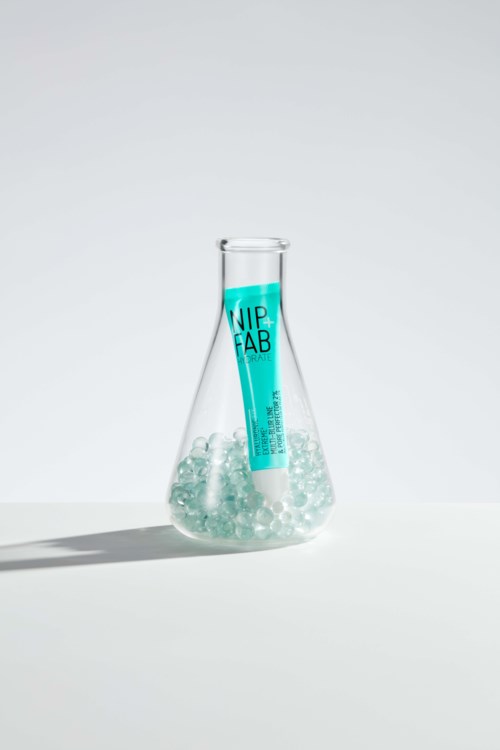 Een proefbuis met blauwe vloeistof in een glazen fles, op een witte achtergrond. De vloeistof lijkt bruisend.
