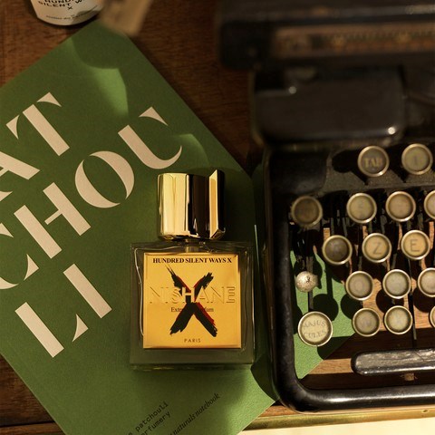 Een parfumfles, een vintage typemachine en een groen boekomslag op een houten oppervlak.