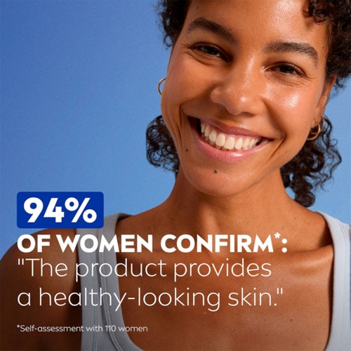 Smiling woman with natural skin, gold earrings, and curly hair, against a blue background, promoting a skincare product.