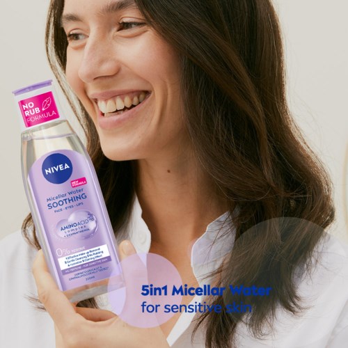 A woman smiling, holding a bottle of Nivea Micellar Water, promoting skincare for sensitive skin.