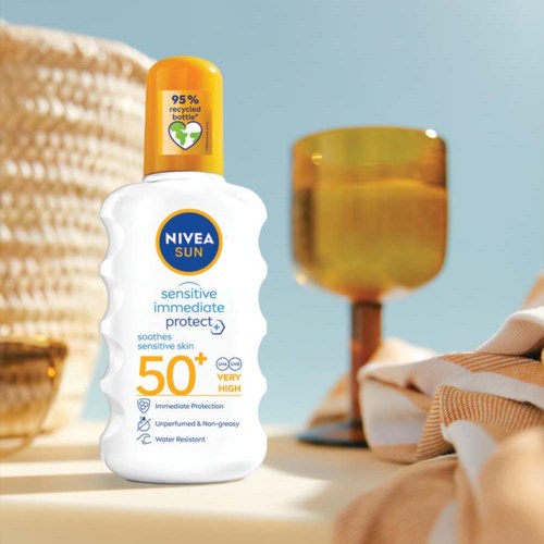 Een witte fles Nivea Sun zonnebrandcrème met 50+ bescherming, op tafel met lamp en doek, zonnige achtergrond.