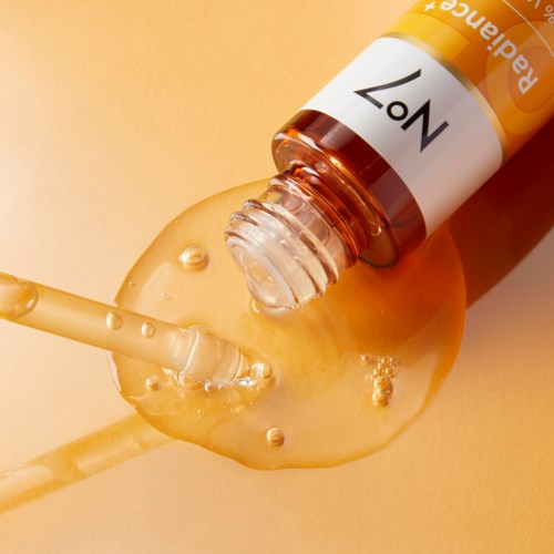 Een druppelflesje met serum, en een druppel serum valt op een oppervlak. Het flesje is gemarkeerd met 'N07'.