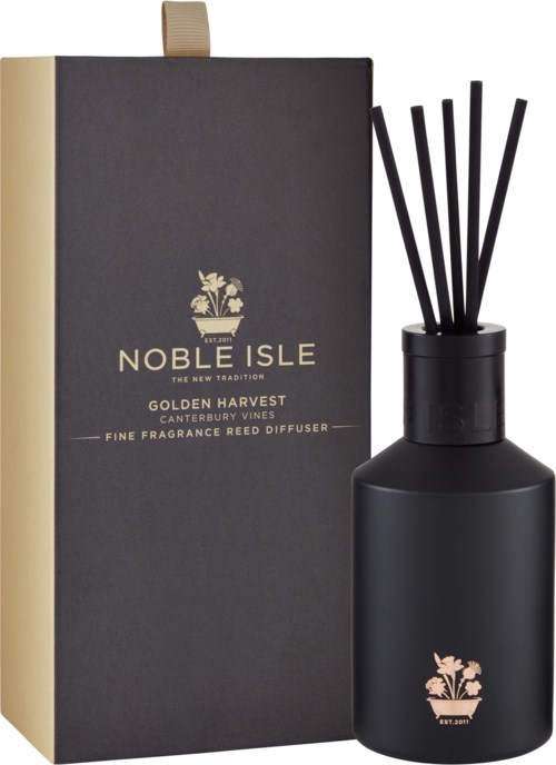 Ein schwarzer Duftdiffusor mit Stäbchen neben einem schwarzen und goldenen Karton mit der Aufschrift 'Noble Isle Golden Harvest.'