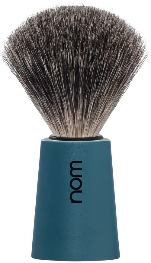 A shaving brush with a blue handle and thick, dark bristles. The handle has the word "nom" on it.