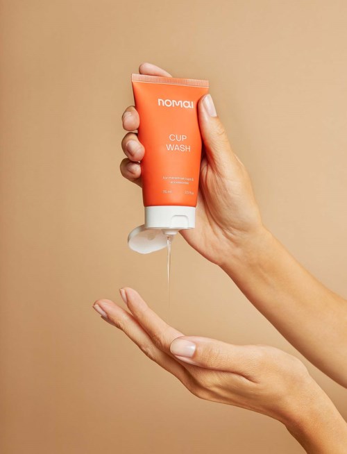 Eine Hand hält eine orangefarbene Tube mit der Aufschrift 'Nomad Cup Wash' und gibt Seife auf die andere Hand.