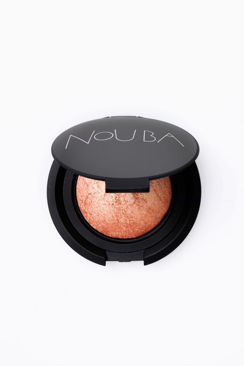 Round makeup compact with a shimmery pink-orange powder inside, covered by a black lid with 'NOUBA' written on it.