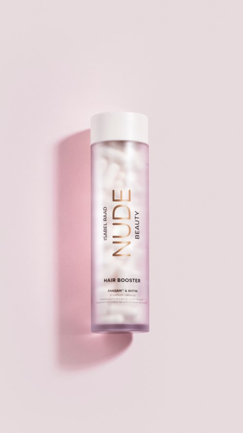 En cylindrisk flaska med vit topp och genomskinlig kropp, märkt 'Nude Beauty Hair Booster', på en rosa bakgrund.