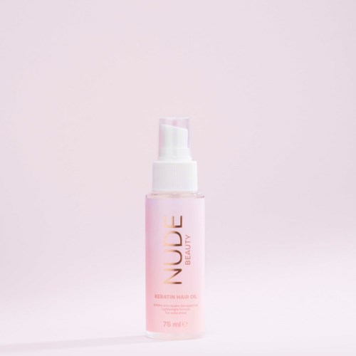 Różowa butelka z napisem "Nuude Beauty Keratin Hair Oil" z pompką na jasnym różowym tle.