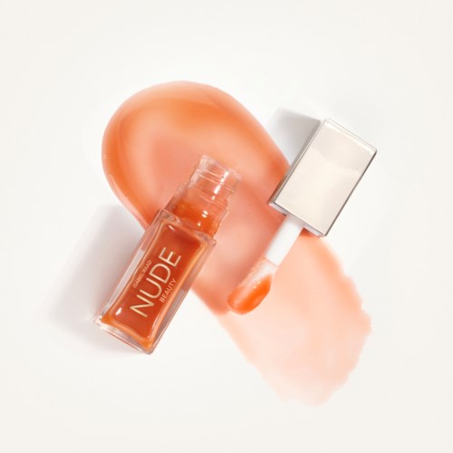 Lip gloss bottle with a light peach color, a peach spot, and some gloss smudge on a white background.