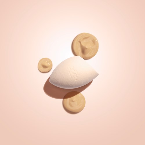 A white makeup sponge with three beige cream swabs on a light background.
