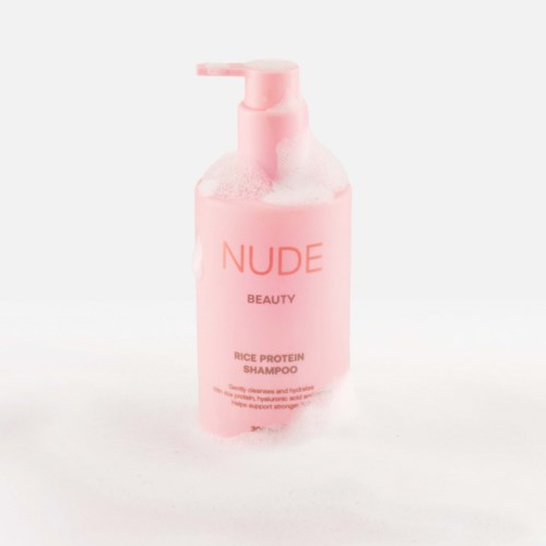 Rosa flaska märkt NUDE Beauty Rice Protein Shampoo med pump, ser ren och enkel ut.