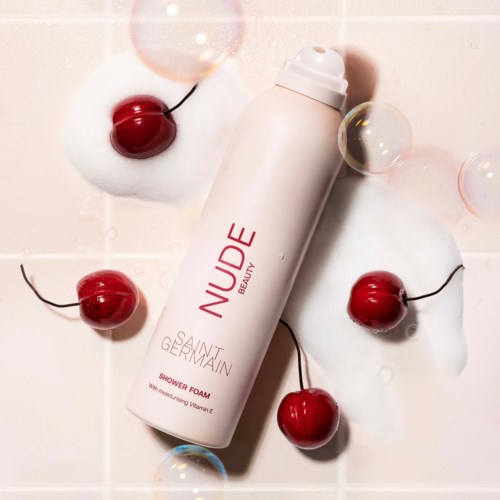 A white bottle labelled 'NUDE' and 'Saint Germain' lying on a tiled surface, with cherries and soap bubbles around.