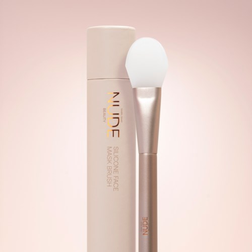Huidverzorgingsproduct met borstel en witte fles met 'NUDE' label voor gezichtsreiniging en make-up verwijdering.