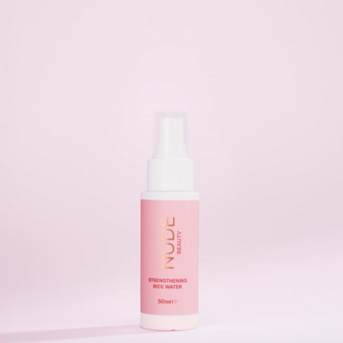 A pink and white bottle labeled Nude Beauty Strengthening Rice Water on a light pink background.