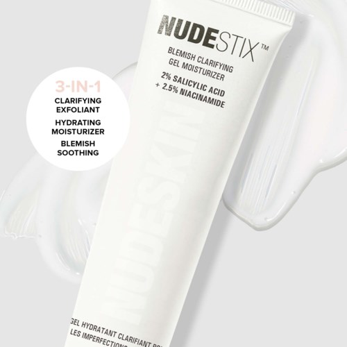 Valkoinen putki, jossa lukee 'NUDESTIX' ja tietoja ihonhoidosta ja ainesosista, vieressä kirkas vesilasi.