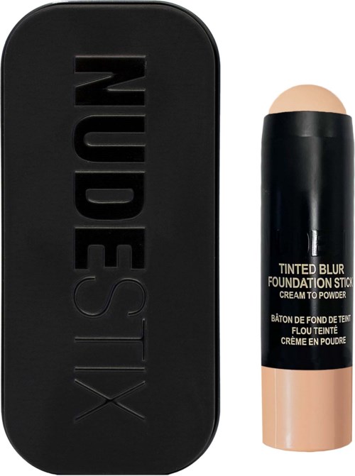 A black makeup palette with the word 'NUDESTIX' on it and a beige-toned stick labeled 'TINTED BLUR FOUNDATION STICK' beside it.