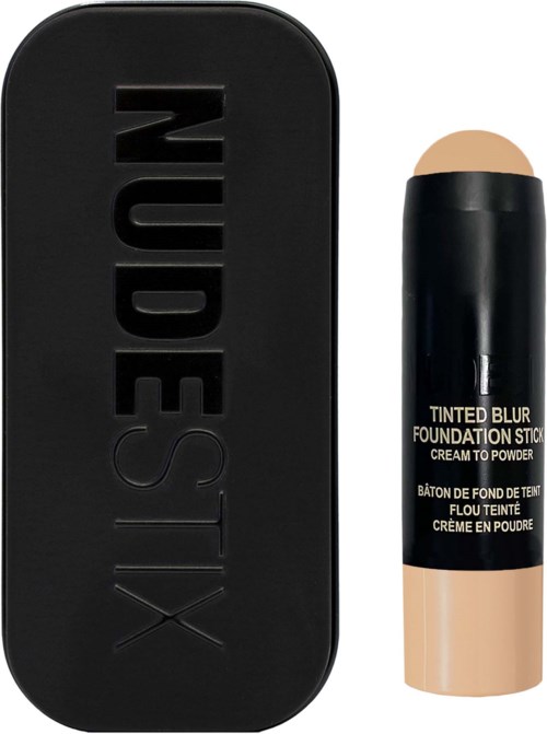 A black compact case with the word 'NUDESTIX' embossed, next to a beige stick foundation with a black cap.