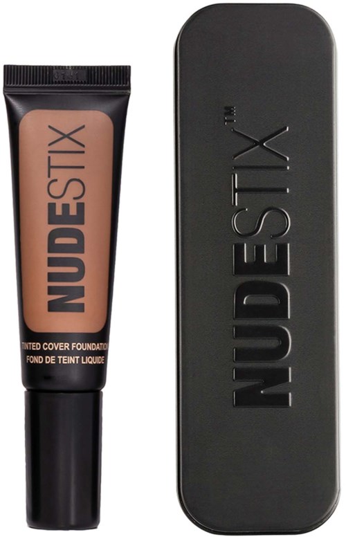 A tube of Nudestix foundation with a black case showing the brand name. The tube is nude-colored and stands beside its box.