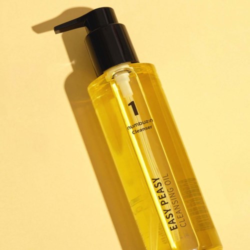 Eine klare gelbe Flasche mit schwarzem Pumpen, beschriftet 'EASY PEASY CLEANSING OIL,' auf gelbem Hintergrund.