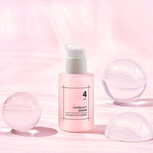 Roze serumfles met pomp, omgeven door heldere glazen ballen op een zachte roze achtergrond.