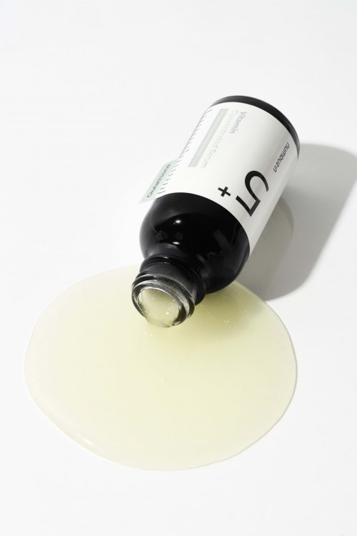 Een zwarte fles met een wit label lekt een gelige vloeistof op een witte ondergrond.