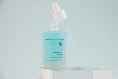 Een blauwe serumbottle met pipetdop, gelabeld '6 Serum, Deep Sleep Mask,' op een witte ondergrond.