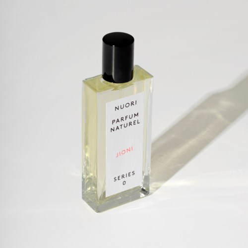 Een kleine parfumfles met een zwarte dop, gemarkeerd 'Nuori Parfum Naturel Joni Series 0', werpt een schaduw.