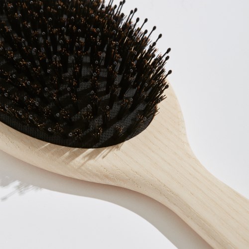 Eine Holzhaarbürste mit schwarzen Borsten. Die Bürste hat einen runden Griff und ist vor einem weißen Hintergrund fotografiert.
